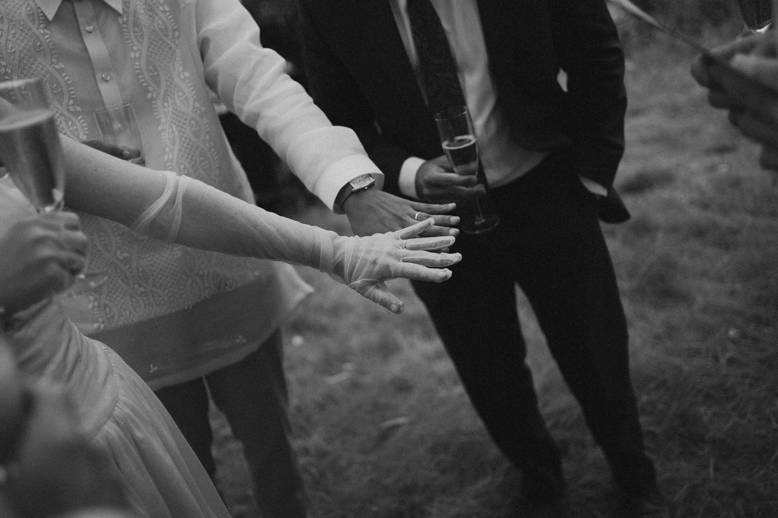 People standing in a line with their hands joined, holding glasses of champagne or wine, at an outdoor social gathering.
