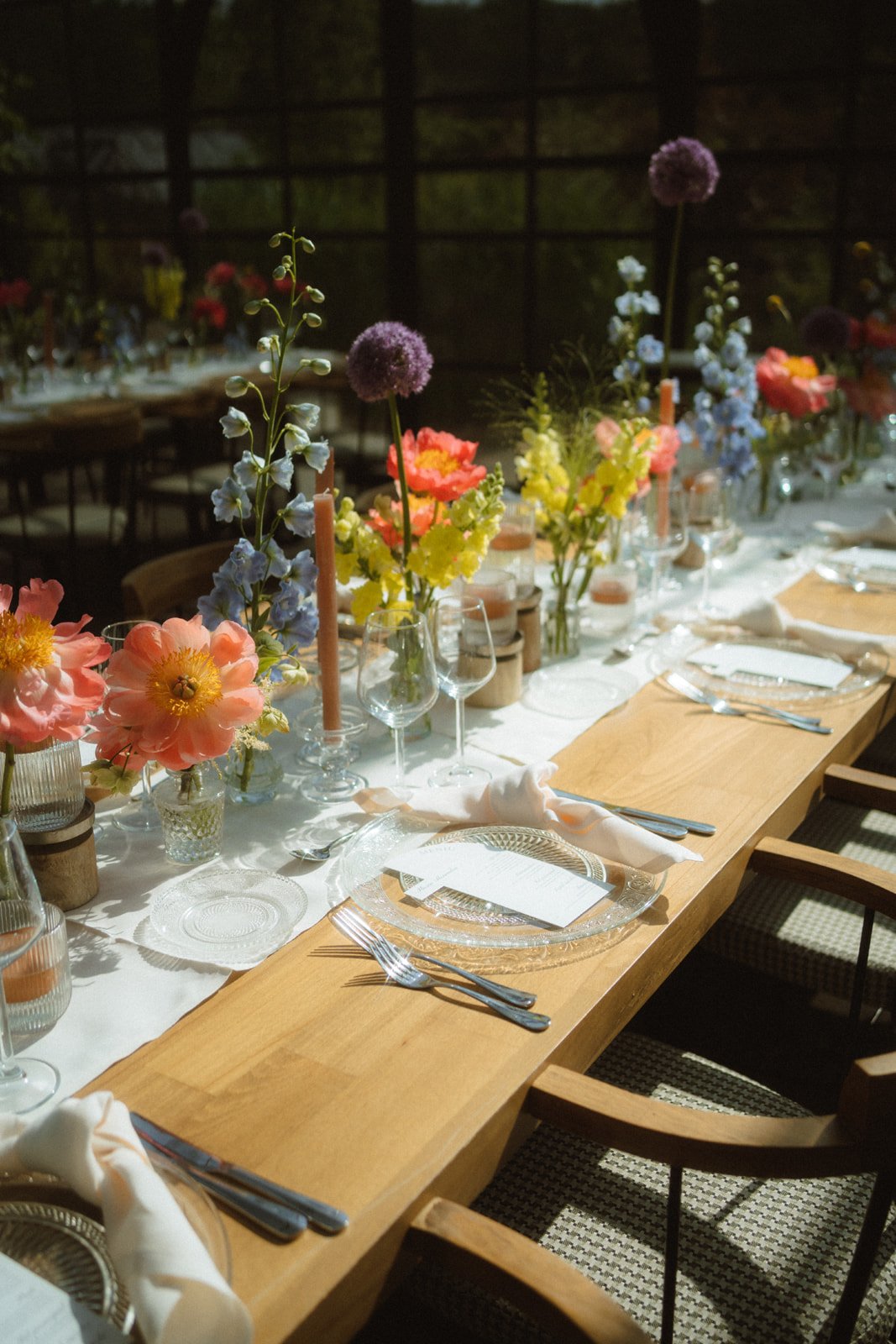 Elegant dining table decorated with colorful flowers, candles, and tableware set for a meal in a dimly lit setting.