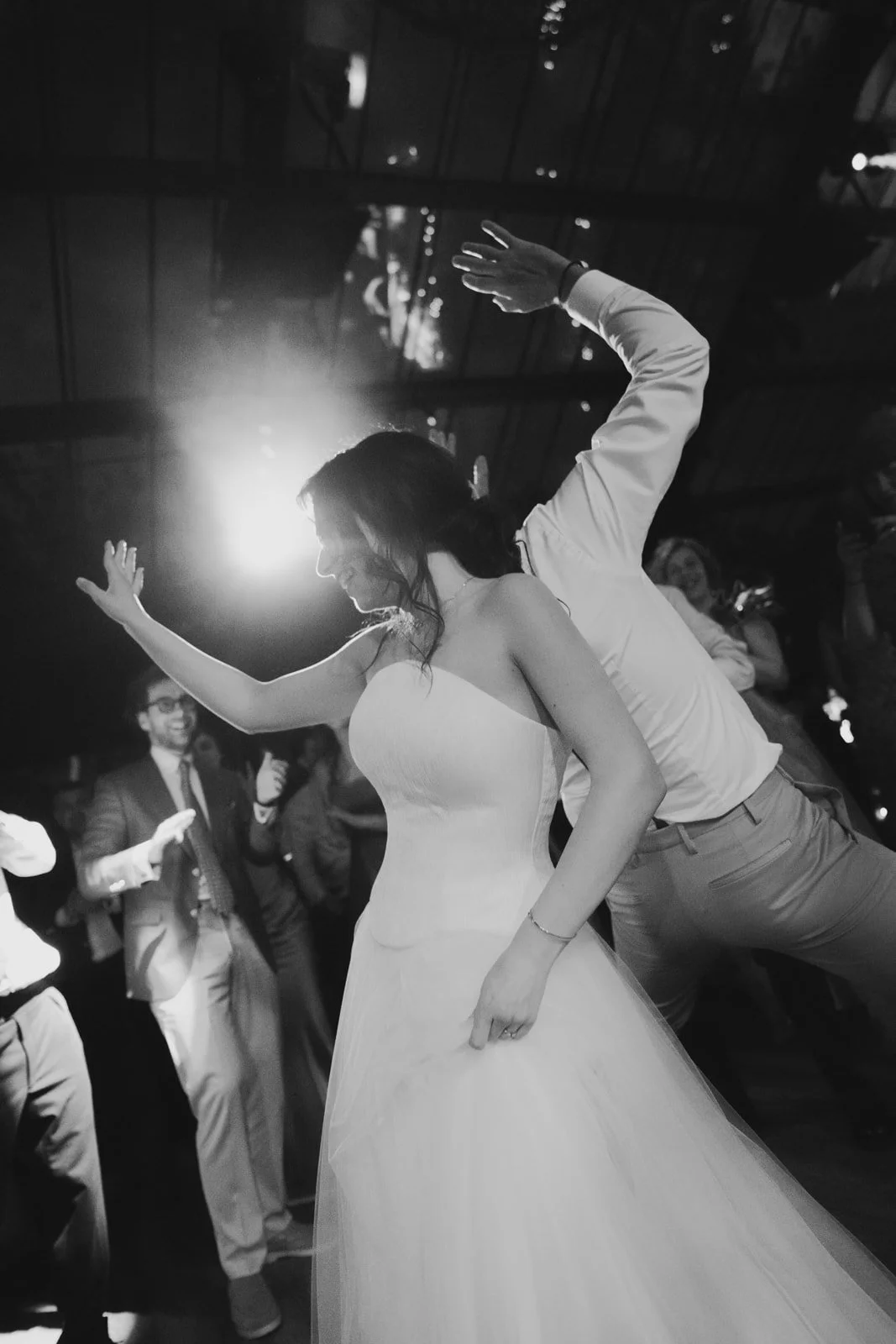 A bride and groom dancing at their wedding reception with guests dancing around them, black and white photo.
