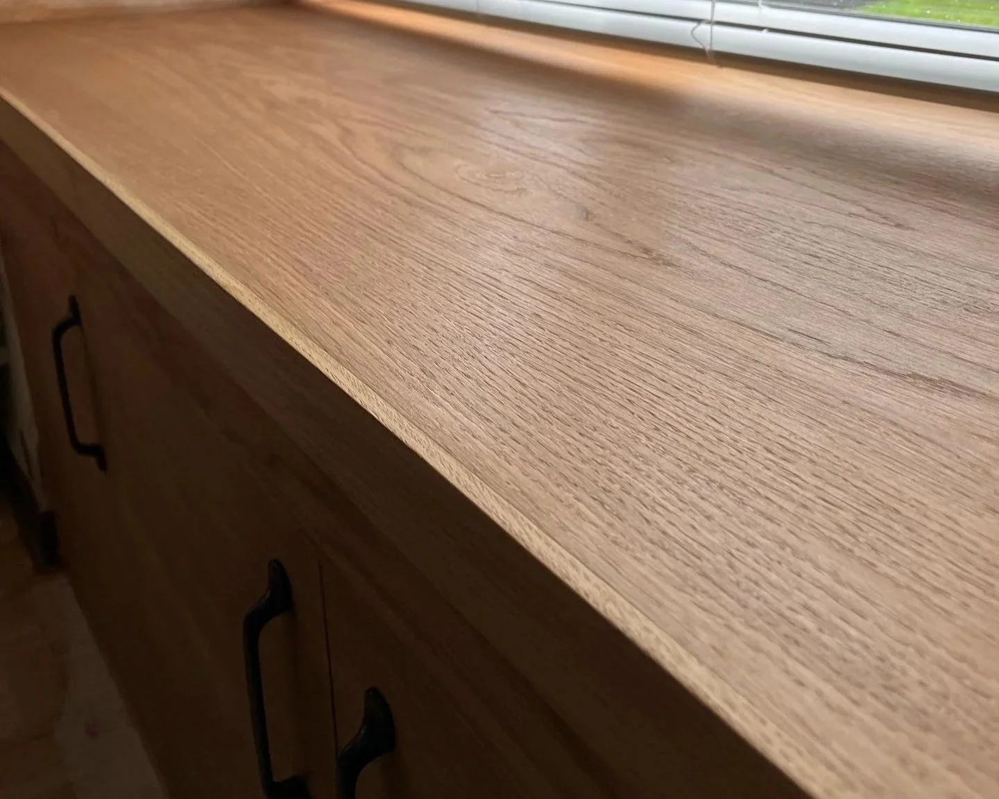 Close-up of a wooden countertop with a window shelf and blinds above.