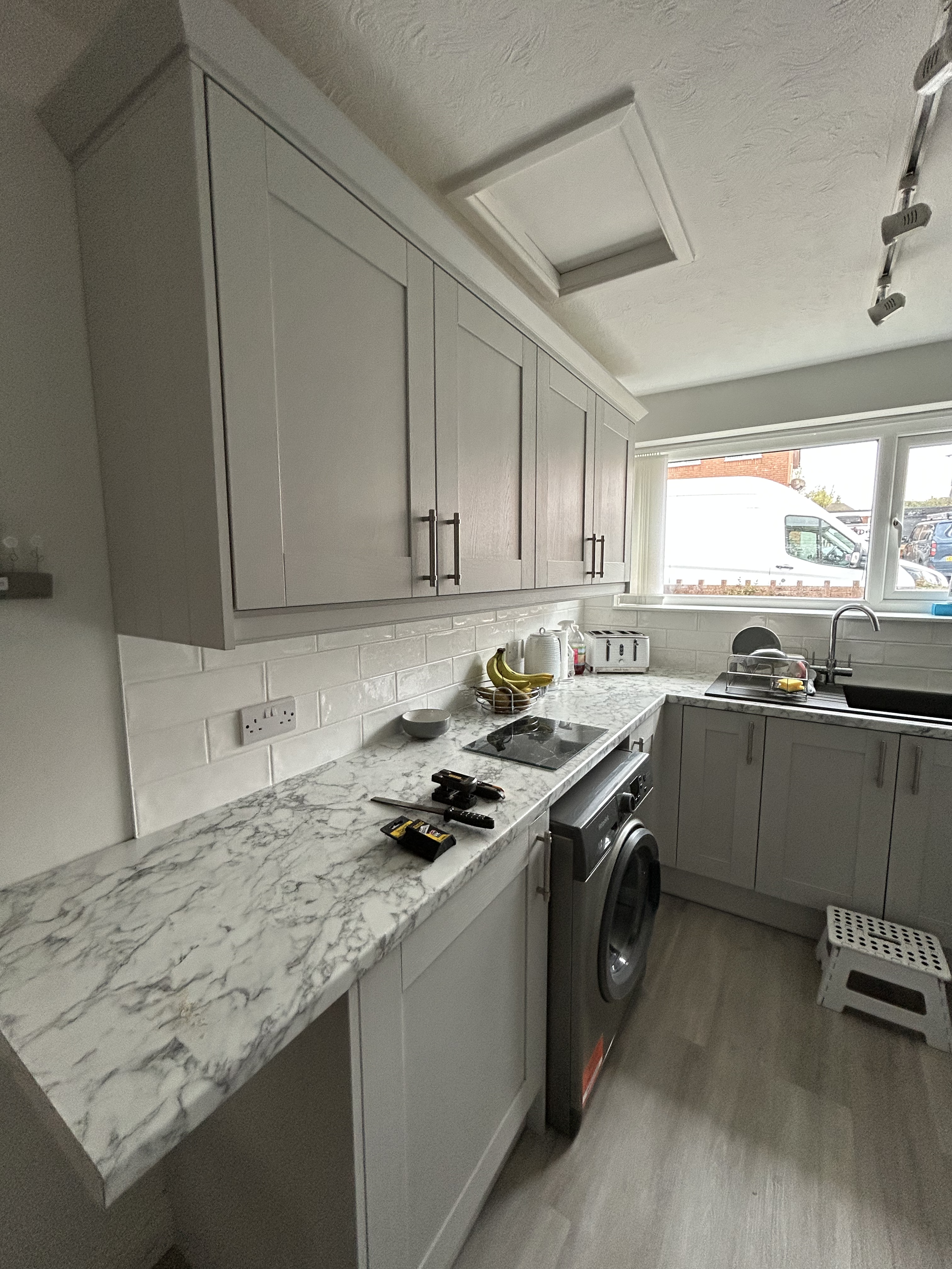 Kitchen with white cabinets, marble countertop, window overlooking a garage, and appliances including a washing machine and toaster.