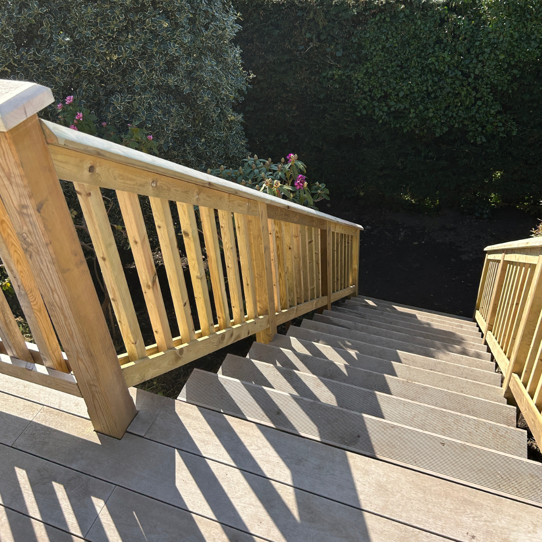 Wooden outdoor staircase casting shadows on a patio, surrounded by green shrubs and flowers.