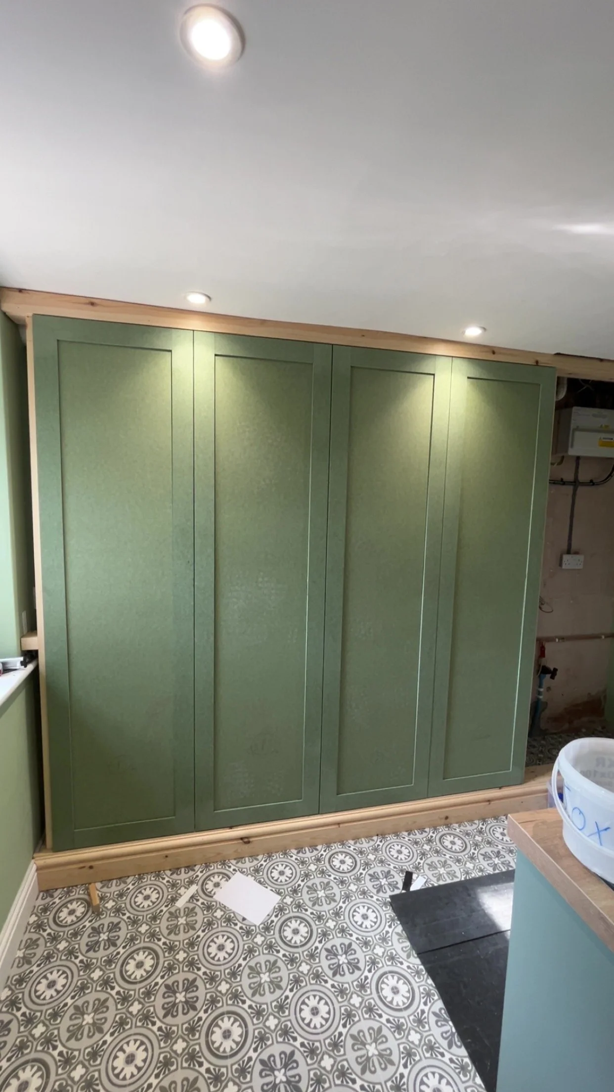 Green kitchen cabinets with a patterned tile floor and ceiling lights.