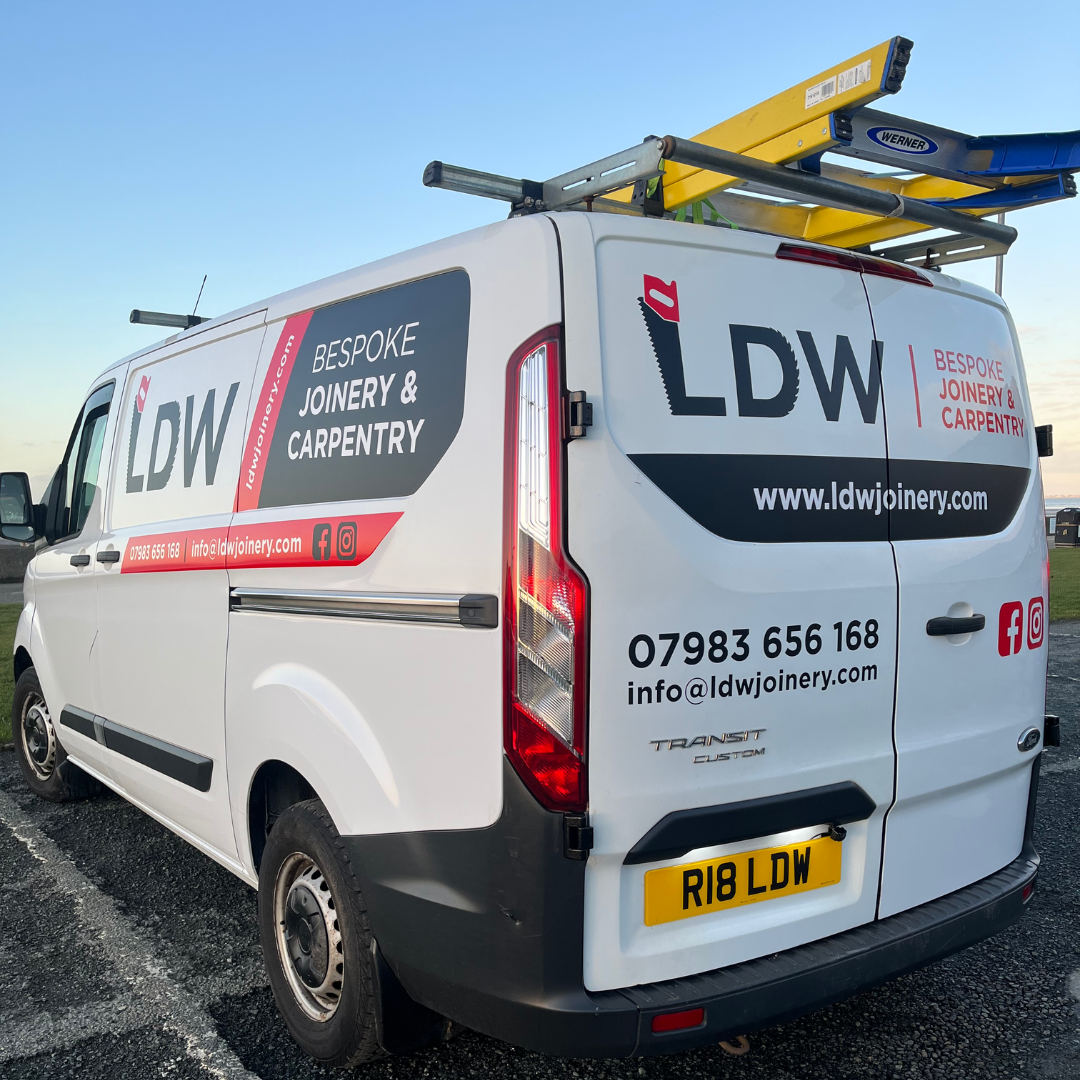 White van with LDW company branding, contact information, and ladder on roof in an outdoor parking lot during dusk.