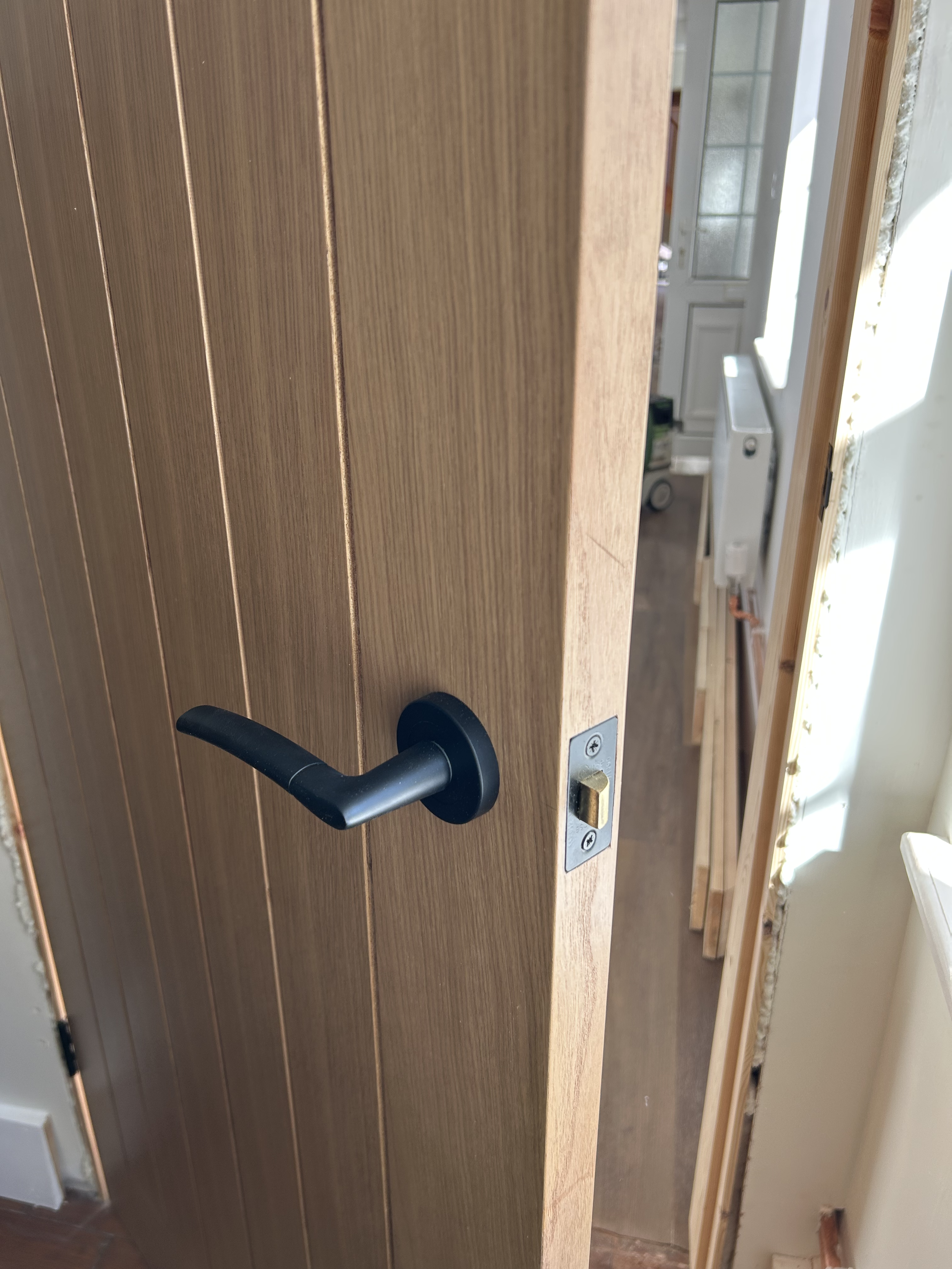 A wooden door with a black handle and a silver lock, open to reveal a kitchen with white cabinets and a window.
