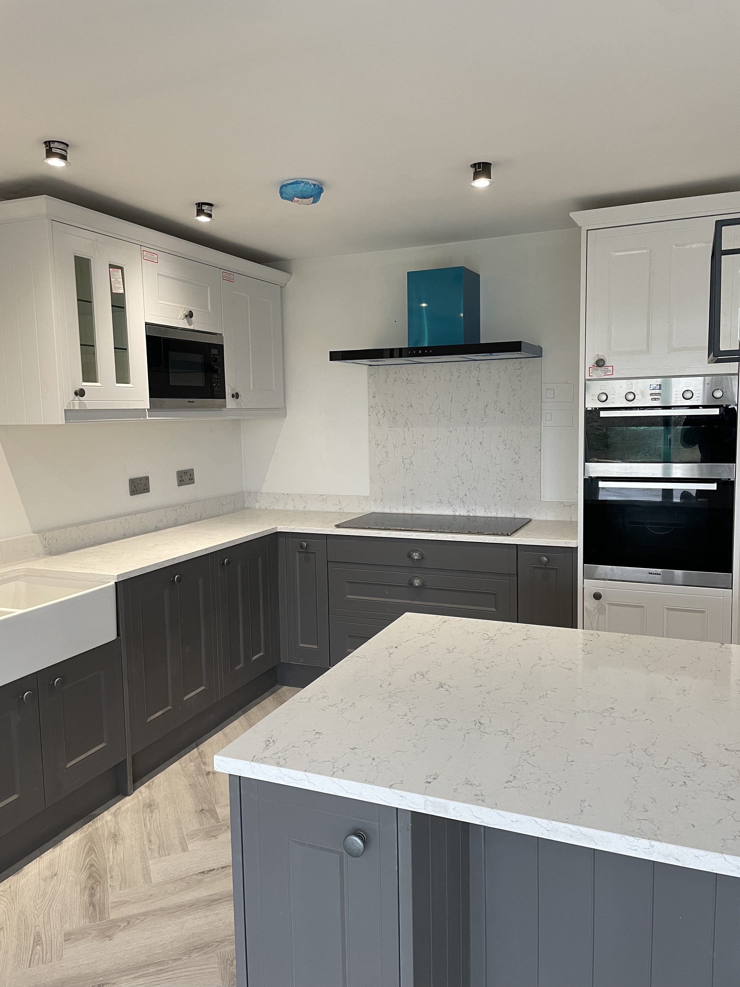 Modern kitchen with grey lower cabinets, white upper cabinets, a white marble countertop, built-in microwave, electric stove, and wood-look flooring.