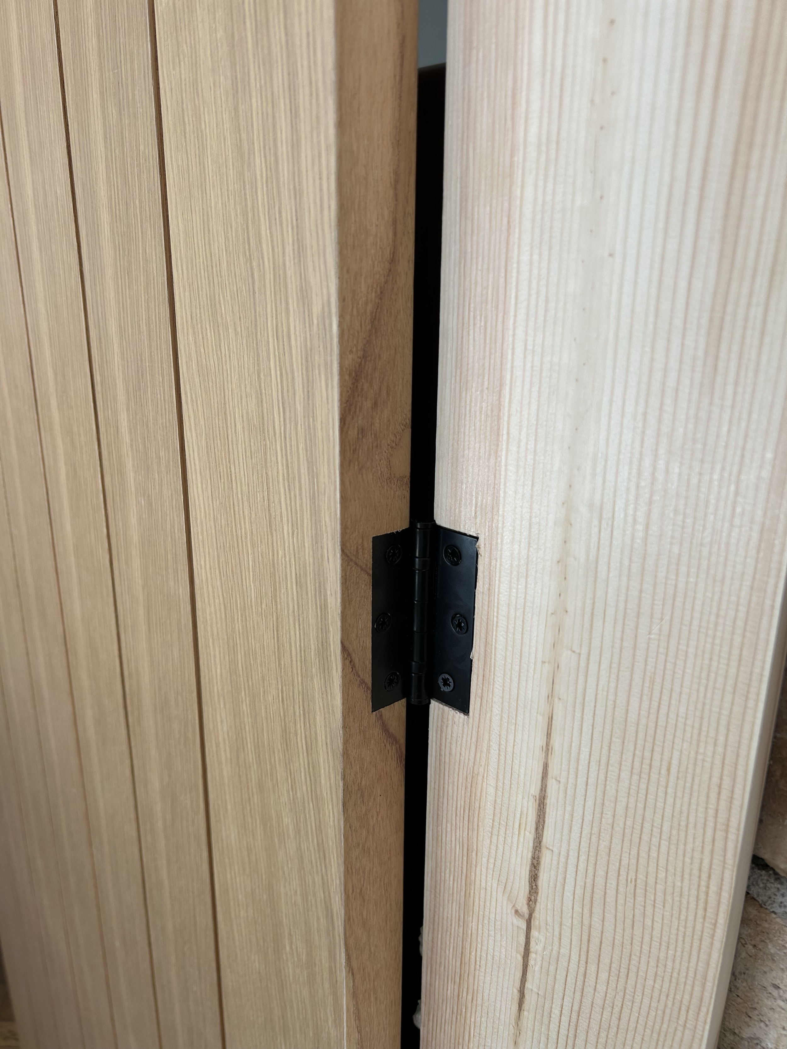 Close-up of a black door hinge attached to light-colored wooden door and frame.