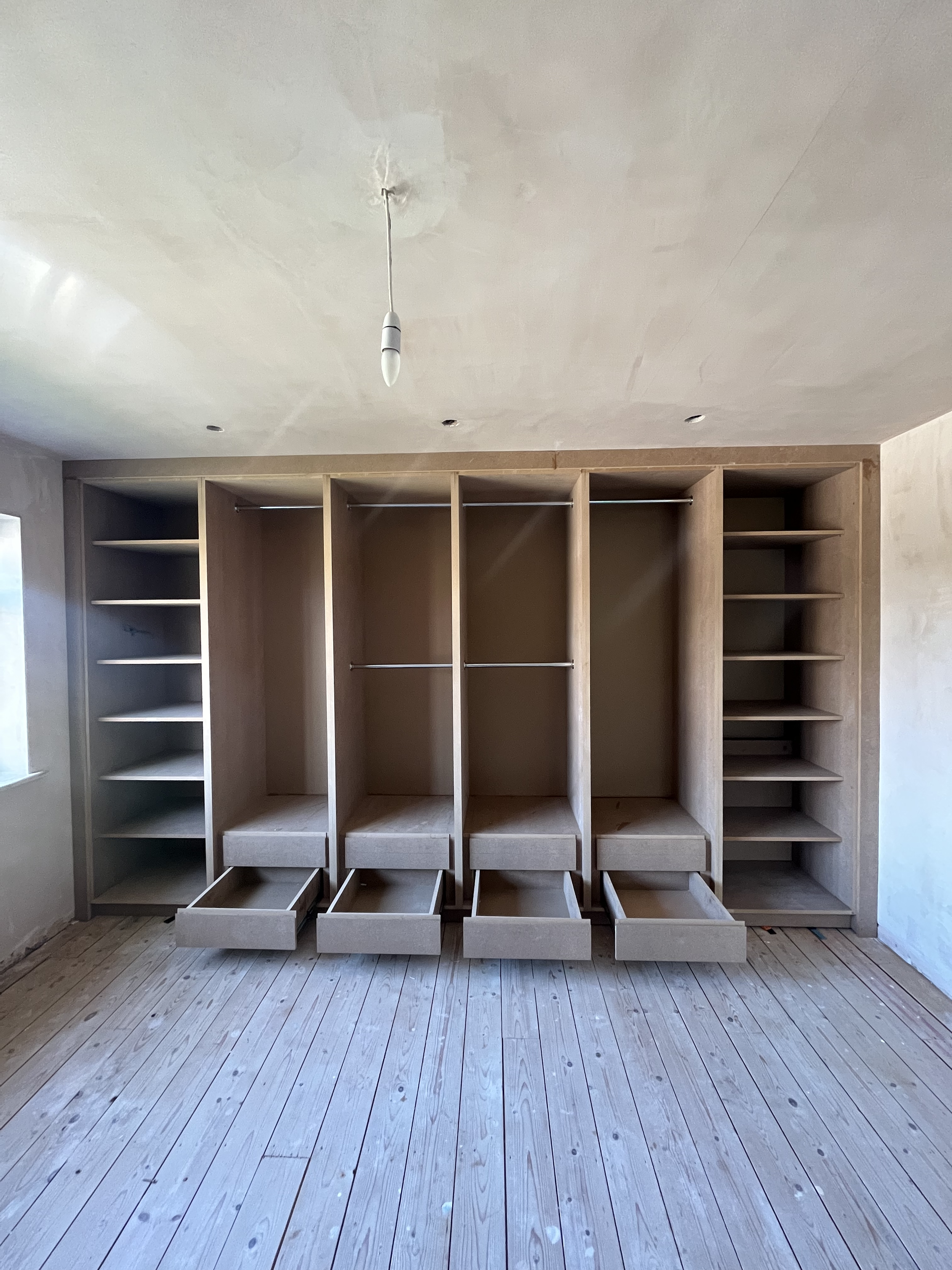 Empty built-in closet with open drawers and shelves in a room with wood flooring.