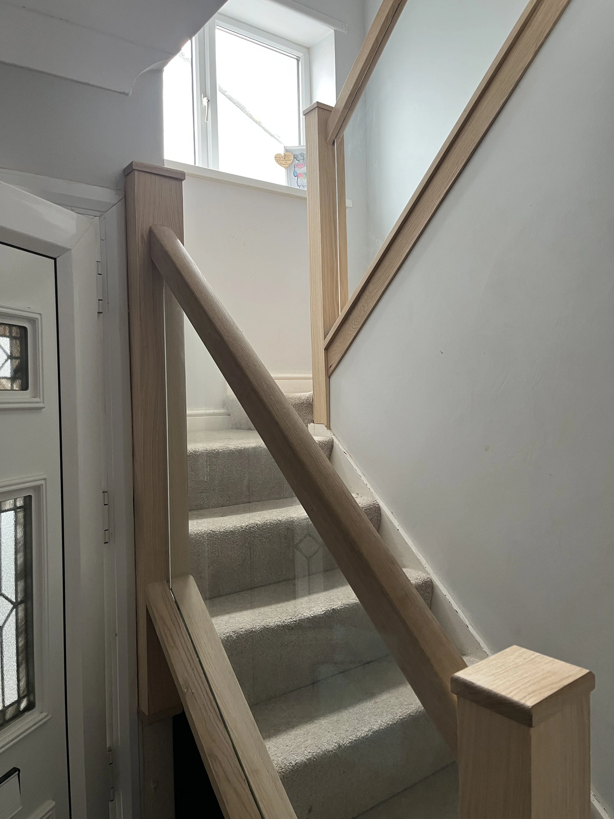 Interior view of a staircase with beige carpeted steps, a wooden handrail, and a window letting in natural light.