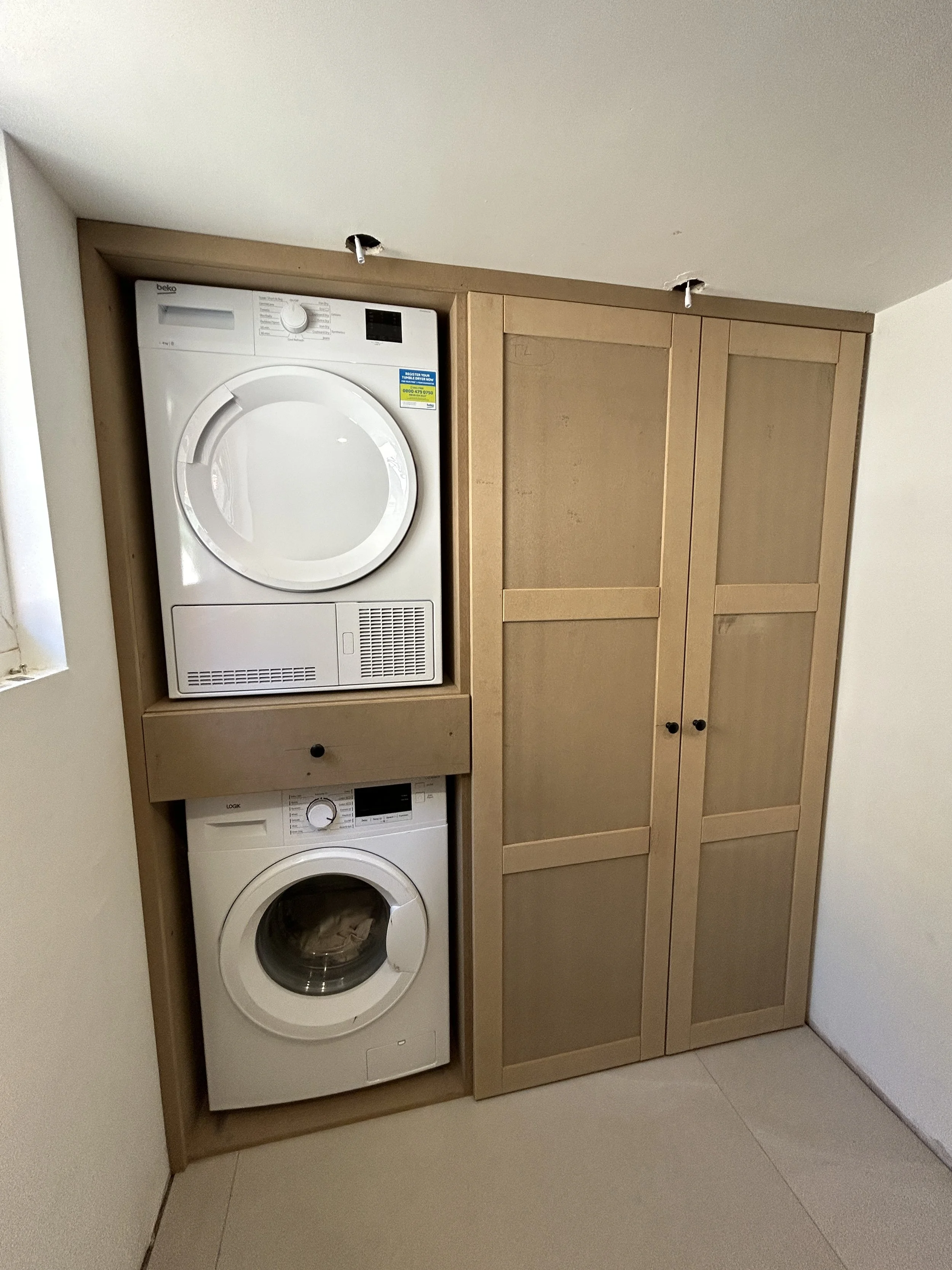 Laundry room with a stack of washer and dryer inside a wooden cabinet, and a tall wooden storage cabinet beside it.