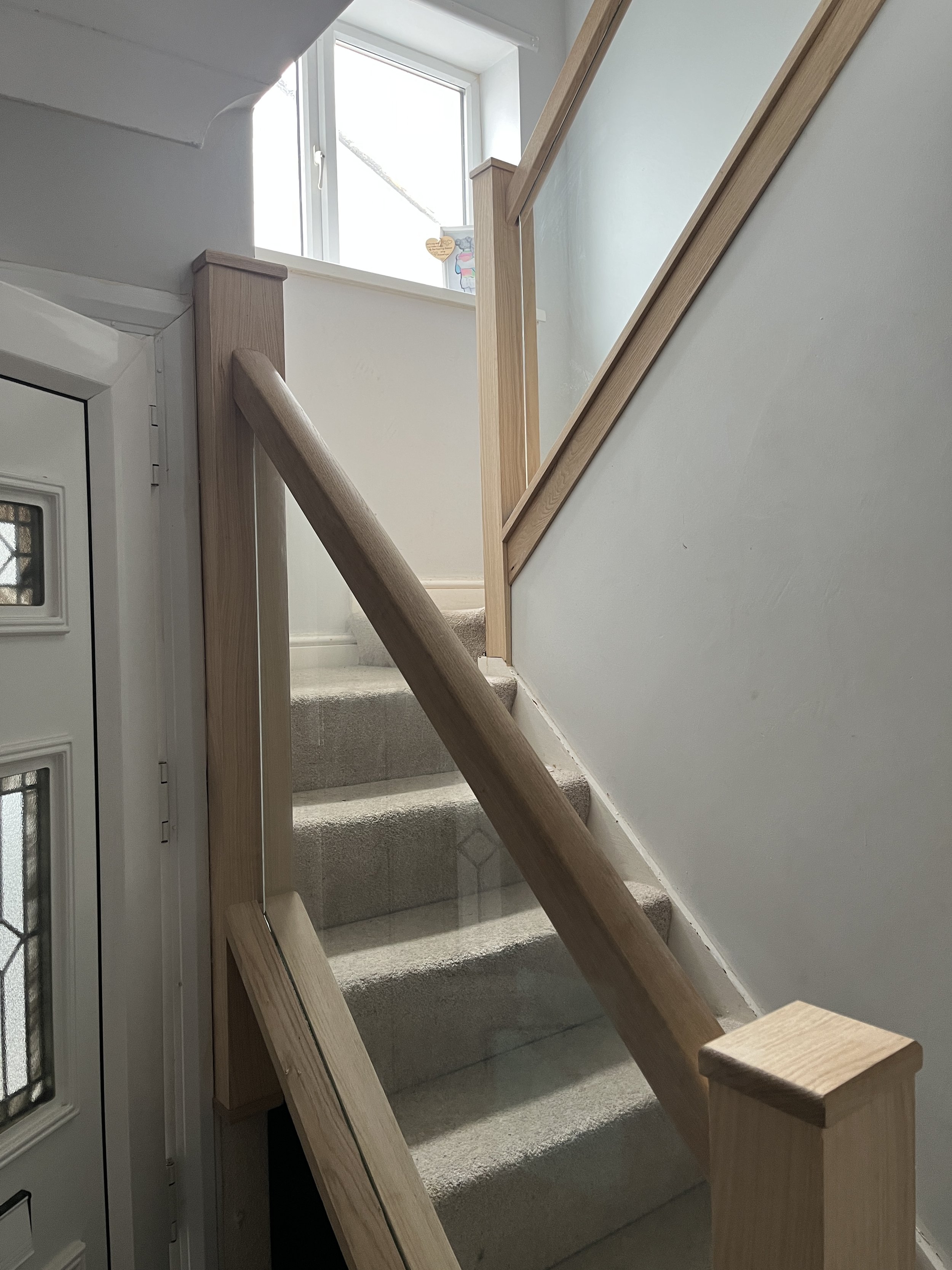 A staircase under construction with wooden handrails and beige carpeted stairs, next to a window letting in natural light.
