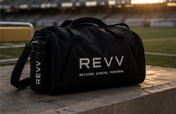 Black sports duffel bag with REVV logo and slogan on a bench near a soccer field at sunset.