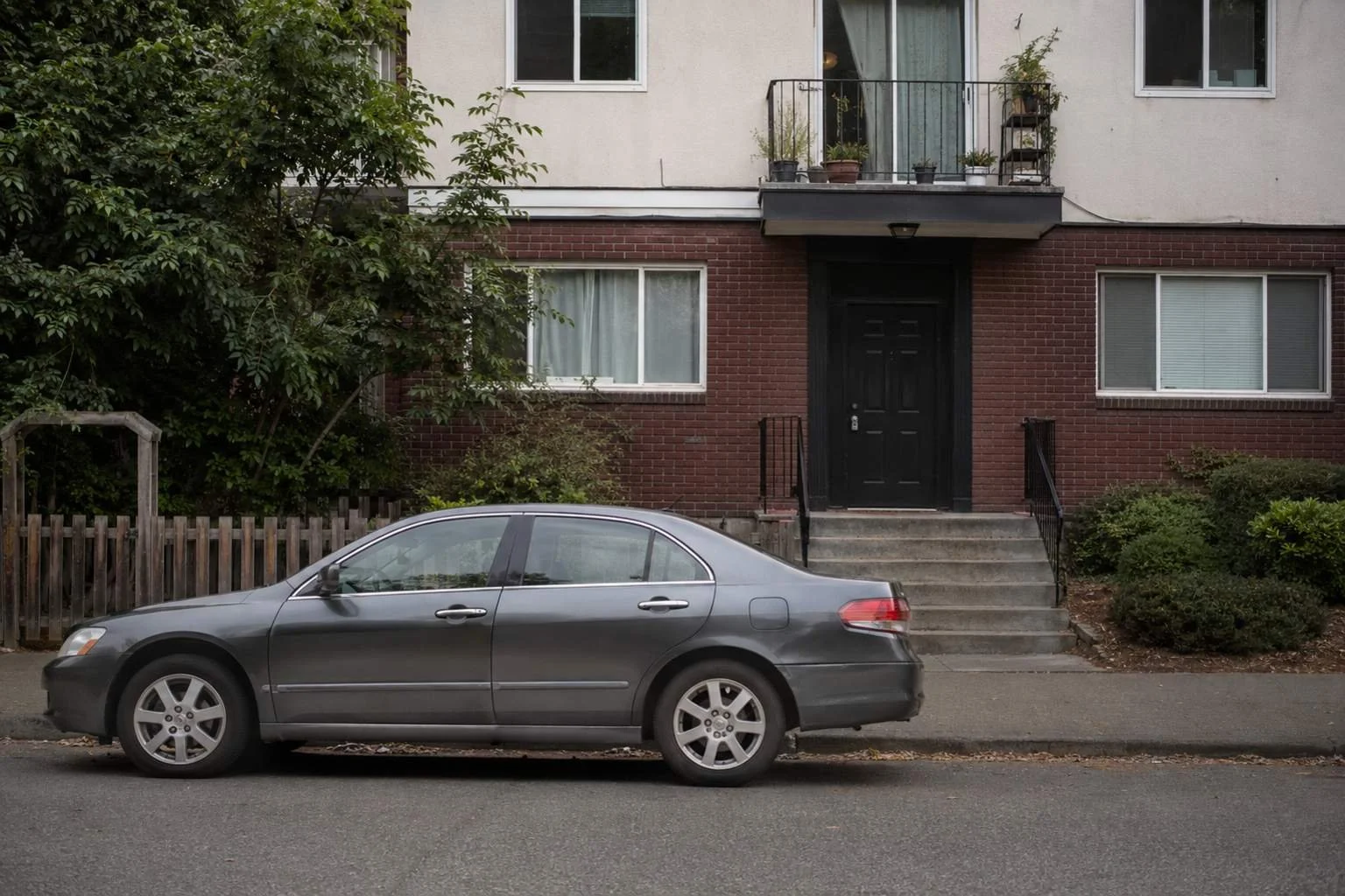 A single unmarked sedan parked at the curb outside a modest brick multi-unit rental building