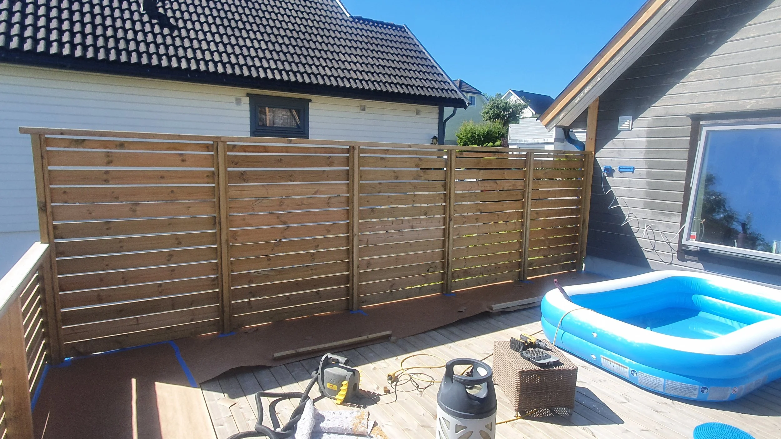 Nylagd tregjerde foran huset på terrasse med lekepool og diverse verktøy og utstyr.