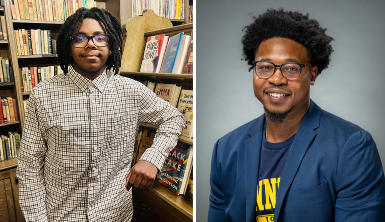 A young person with glasses and dreadlocks standing in a bookstore next to a bookshelf filled with books. Another person with glasses and curly hair wearing a blue blazer and a dark shirt with yellow text, smiling against a plain background.