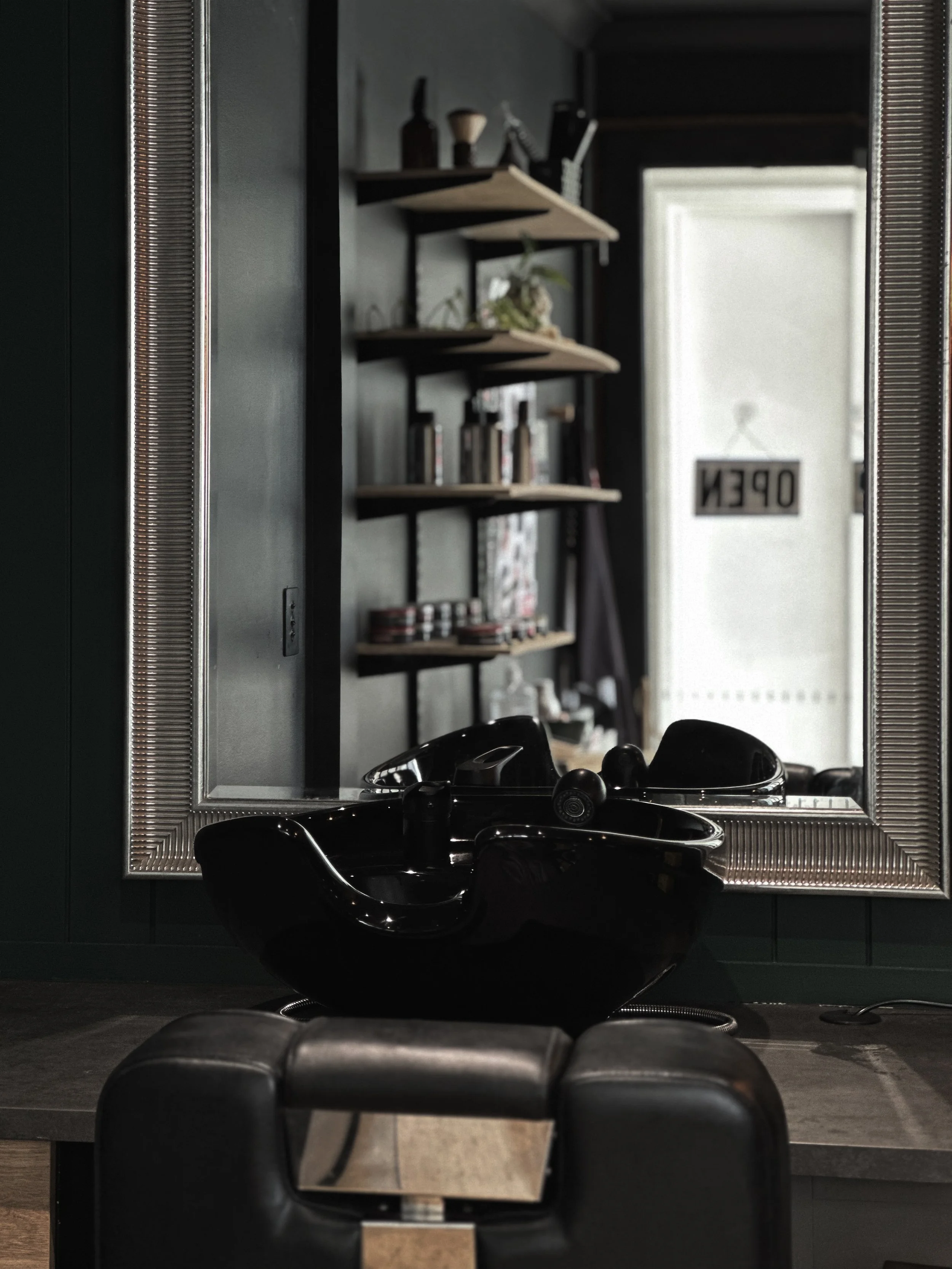 A mirror reflecting a room with dark walls, shelves with books and decorative items, a door with a sign that says 'OPEN', and a black bowl on a surface in the foreground.