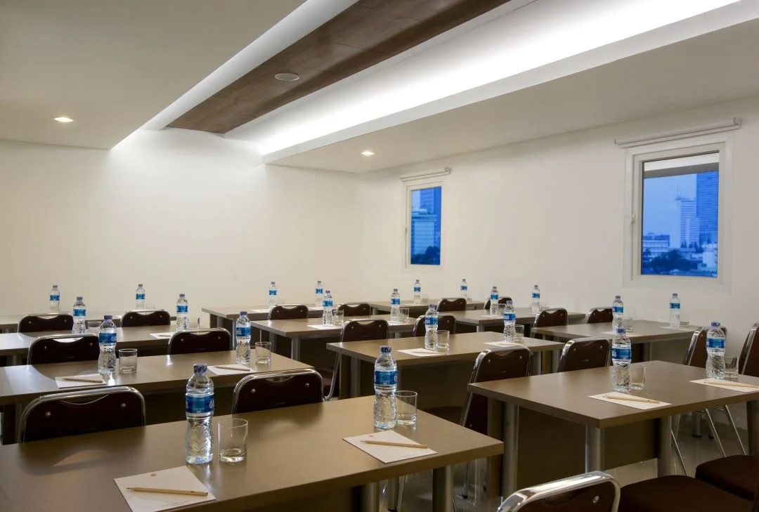 a meeting room with two windows, with a bottle and a glass on every chairs and desks in it.