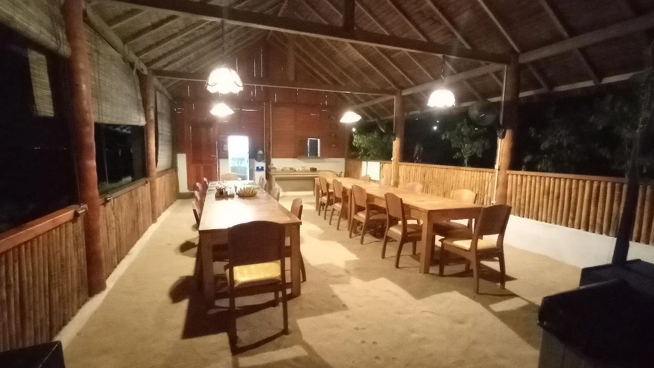 A dining room in a diving resort with woods, ratans walls and furnitures combined, and a roof made of bamboo leaves.