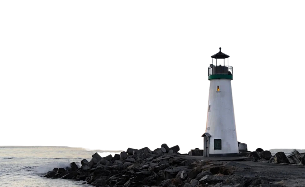White lighthouse with a dark green railing and black lantern room, standing on a rocky breakwater at dusk
