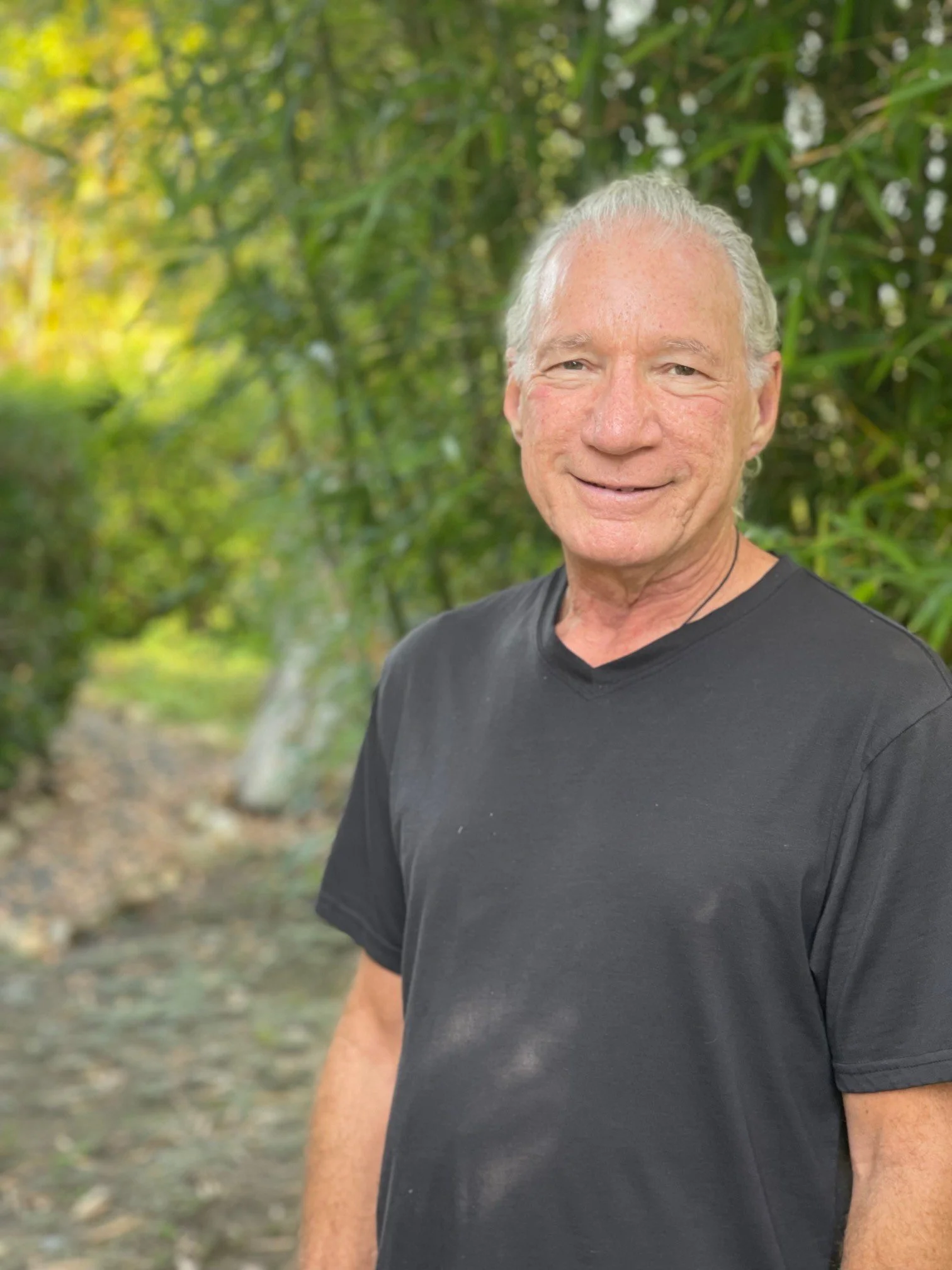 Ben Cohen, Ph.D. smiling outdoors with green foliage background, wearing a black t-shirt.