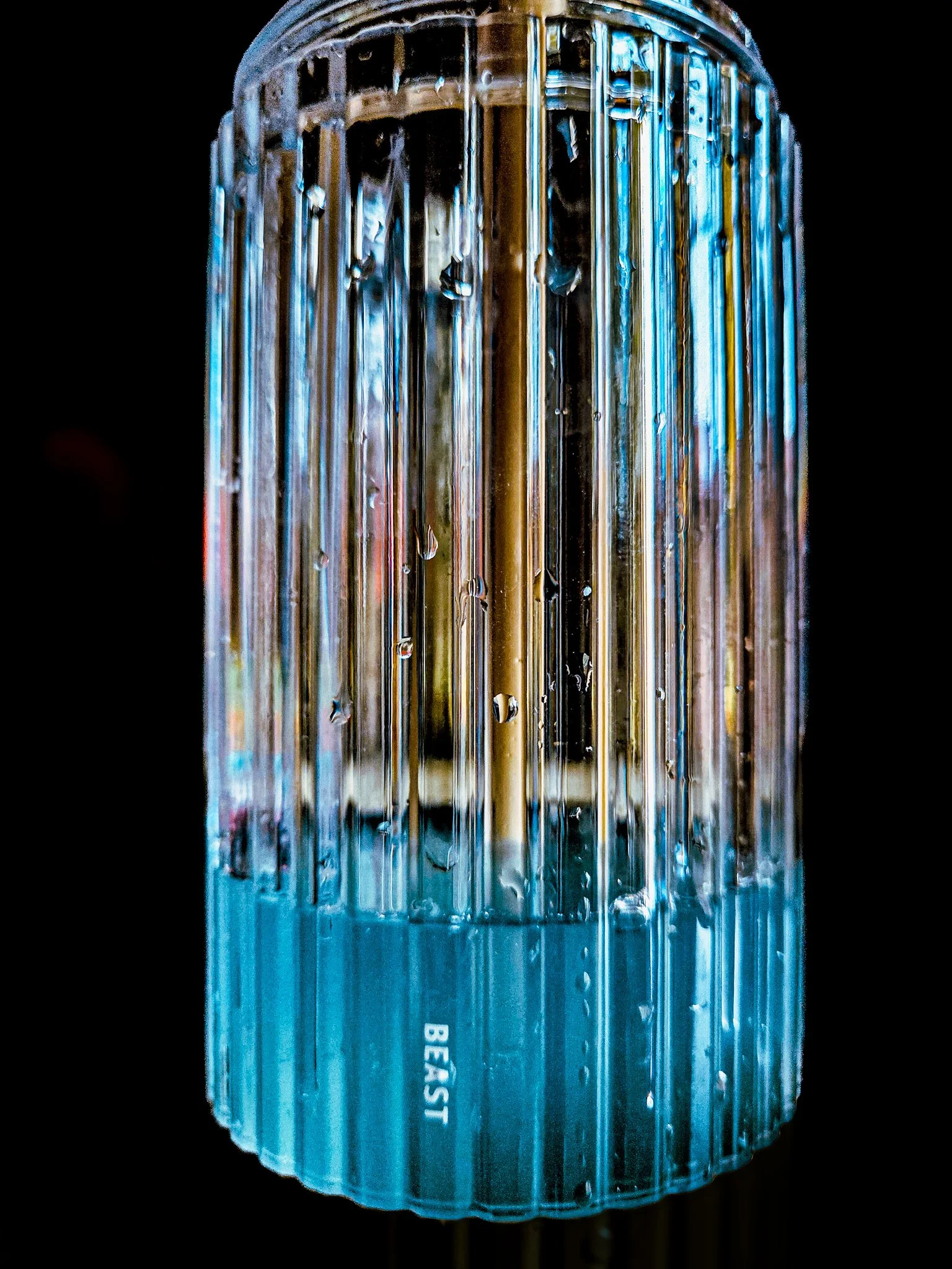 Close-up of a blue-tinted glass bottle with vertical ridges and water droplets, labeled 'BEAST' at the bottom.