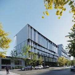 Modern multi-story office building with glass windows, surrounded by trees and parked cars in front.