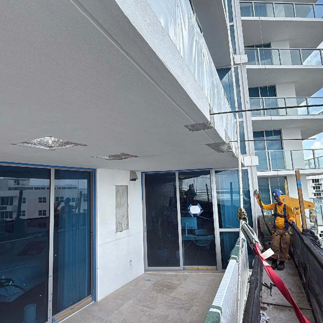 Construction worker in yellow safety gear and blue helmet standing on balcony of a building under construction.