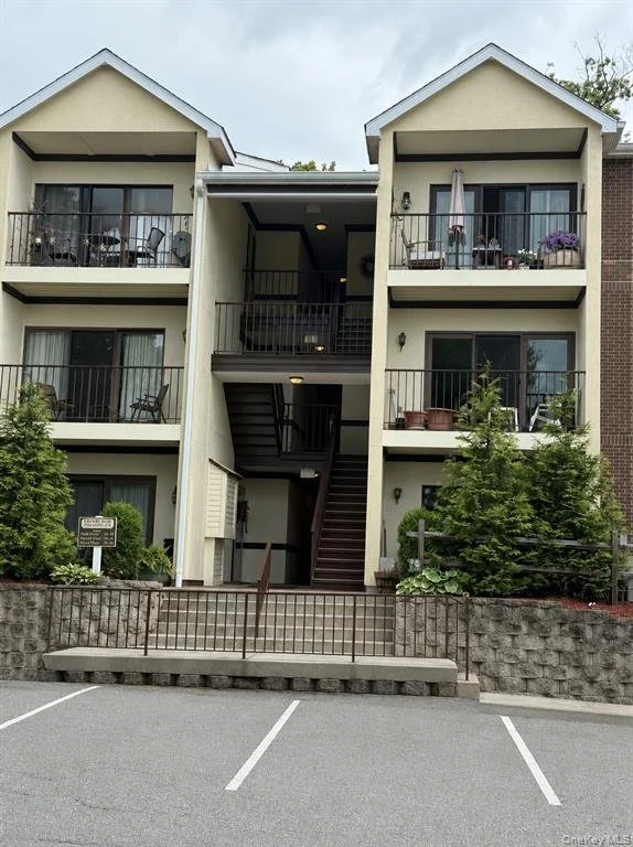 Three-story apartment building with balconies, stairs, and parking lot in front