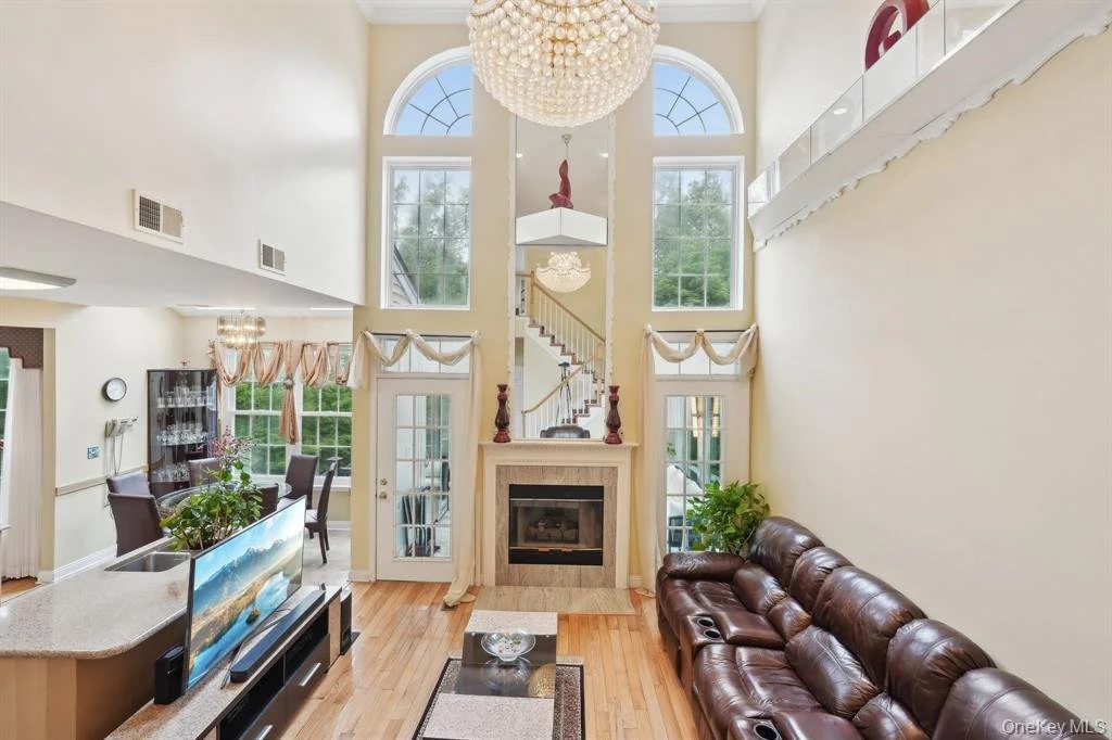 Interior view of a spacious living room with high ceilings, large windows, a centered fireplace, and a leather sofa.