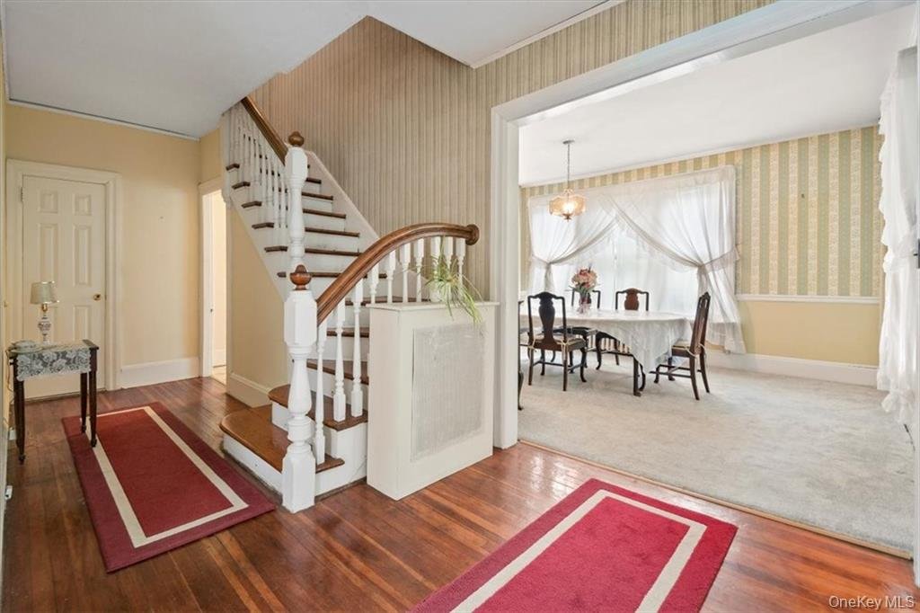Interior of a house showing a staircase, a hallway, and a dining room with a table, chairs, curtains, and a chandelier.
