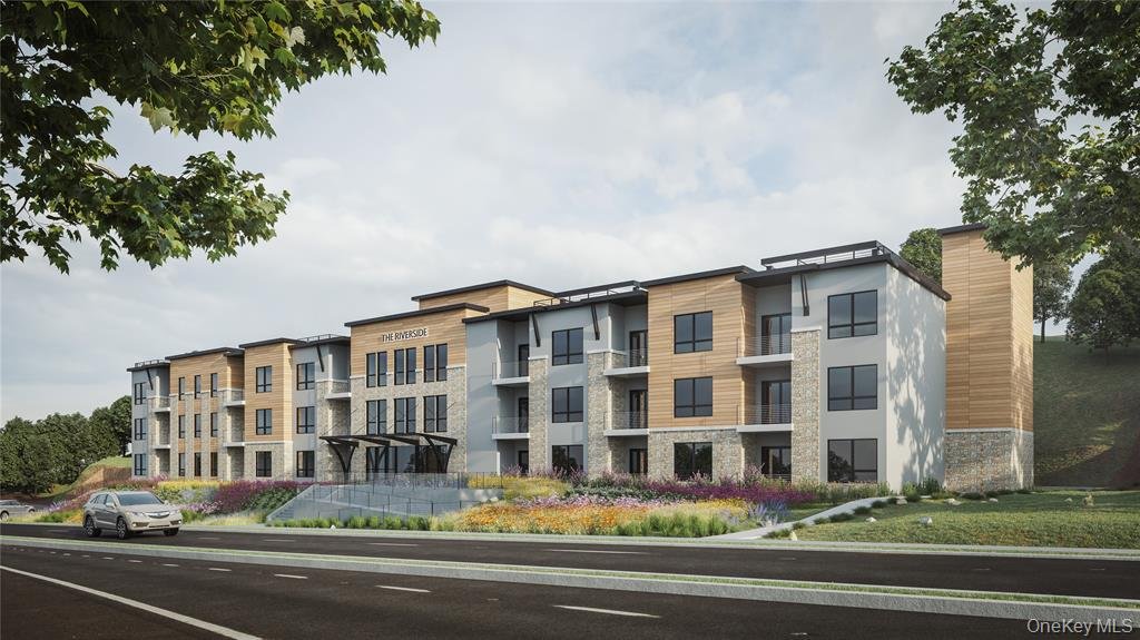 A modern multi-story apartment building named 'The Riverside' with large windows, balconies, and a landscaped area with flowers in front. The building has a combination of wood, stone, and white exterior finishes, and is situated on a street with tre