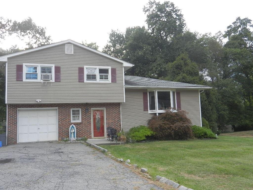 Two-story house with brick and vinyl siding, white garage door, front door with decorative glass, bay window, and purple shutters, surrounded by a lawn and trees in the background.