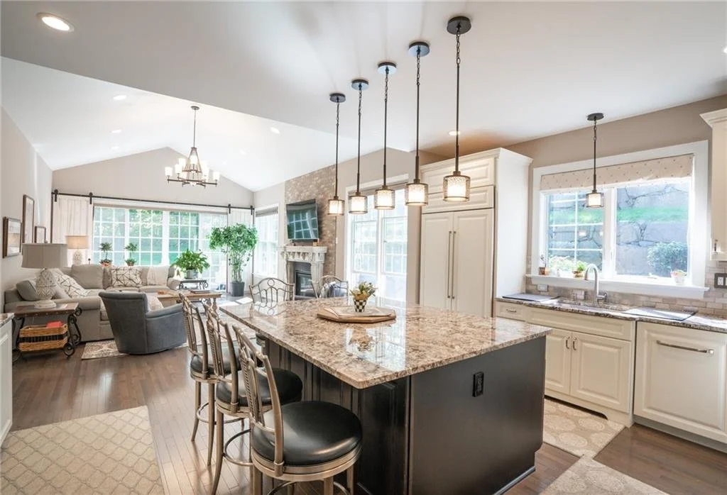 Open-concept living room and kitchen with granite island and hanging pendant lights.