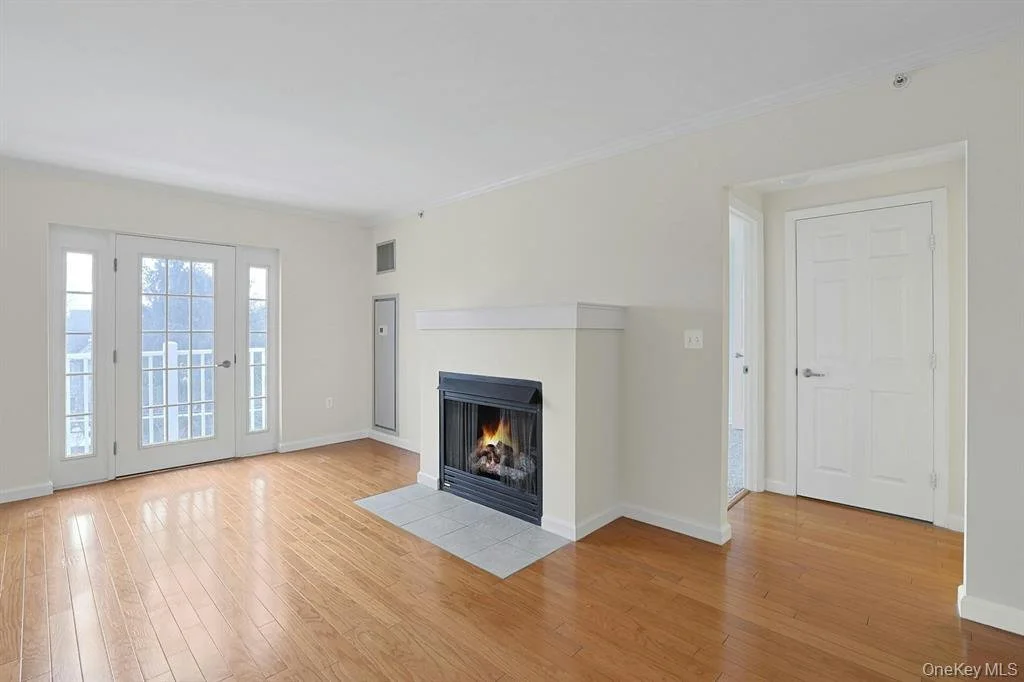 Empty living room with wood flooring, white walls, a fireplace, and French doors leading outside.