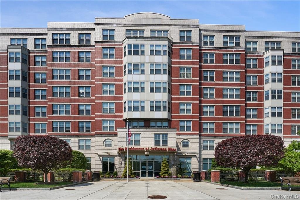 Front view of a multi-story apartment building with brick and beige facade, landscaped entrance with bushes and trees, and a sign that reads 'The Atlantean on Jaffenham House'.