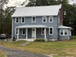 Three-story blue house with white trim, metal roof, front porch, and an American flag.