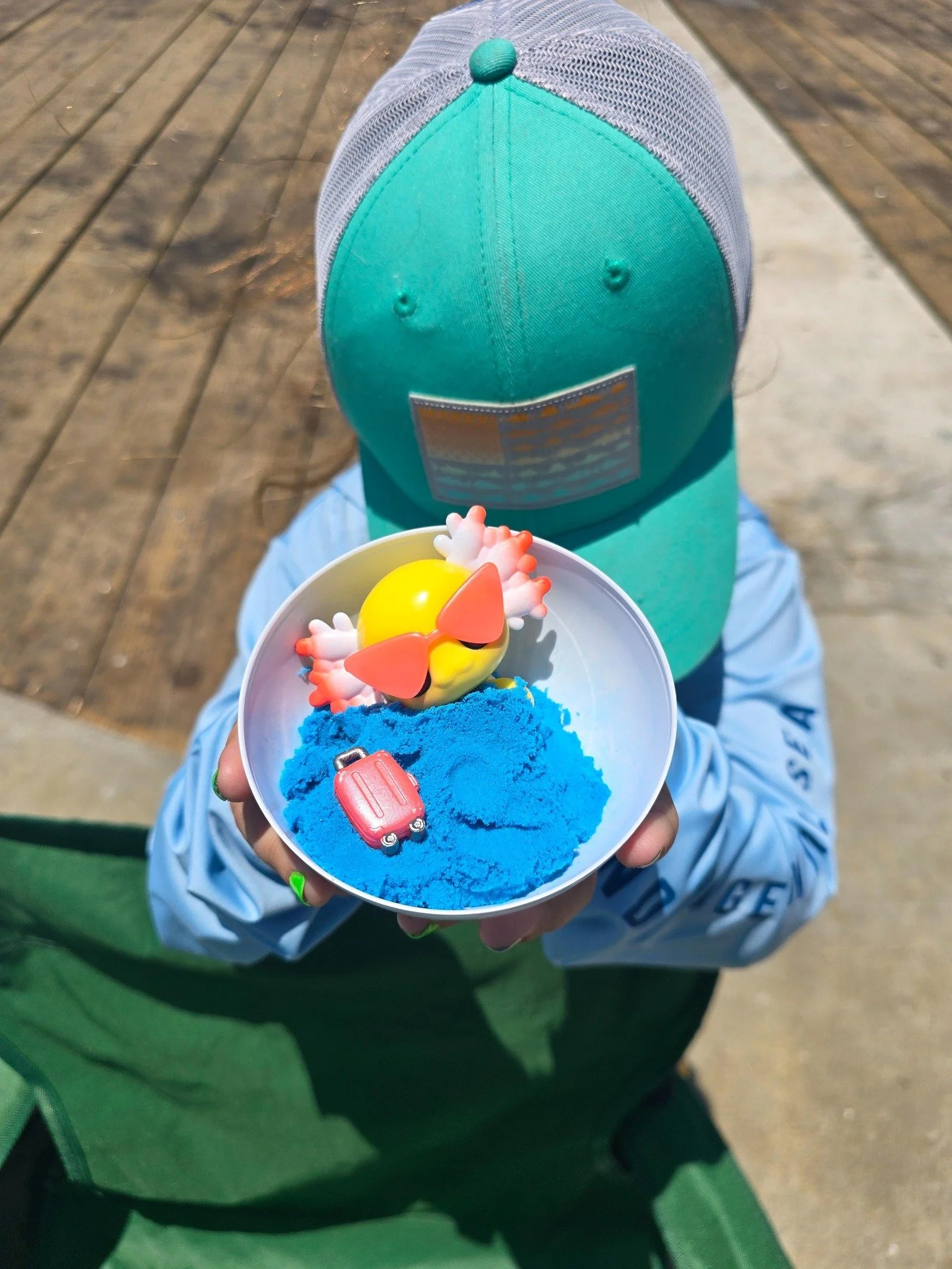 Child holding the original axolotl toy that inspired Relaxalotl, featuring sunglasses, beach sand, and a miniature travel-themed play scene.