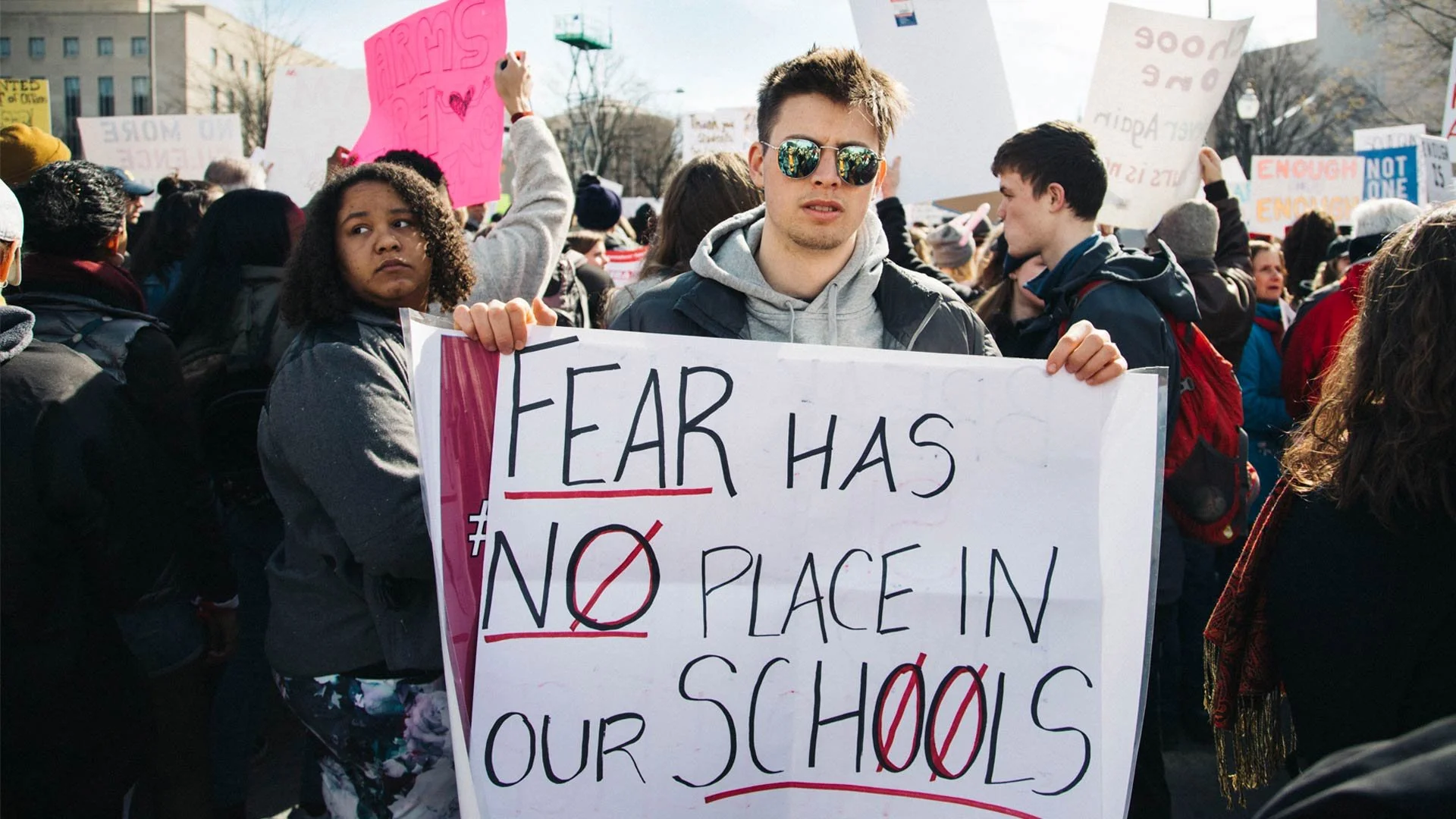 A photo of a person holding a sign at a protest that says, "Fear has no place in our schools."