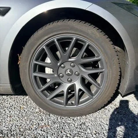 Een close-up van het voorwiel van een elektrische auto, inclusief de wielrand en band, met een gravel ondergrond.