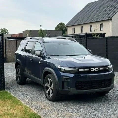Een blauwe SUV geparkeerd op een gravel oprit met tuin en modern huis op de achtergrond.