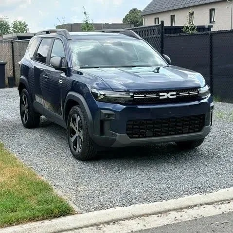 Donkere blauwe SUV geparkeerd op grind voor een omheinde tuin met moderne woning erachter.