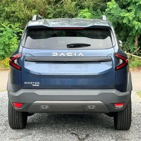A blue Dacia Bigster SUV geparkeerd op een_grindweg met groene bomen op de achtergrond.