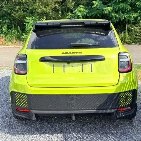 De achterkant van een felle groene Abarth auto op een parkeerplaats met groene struiken op de achtergrond.