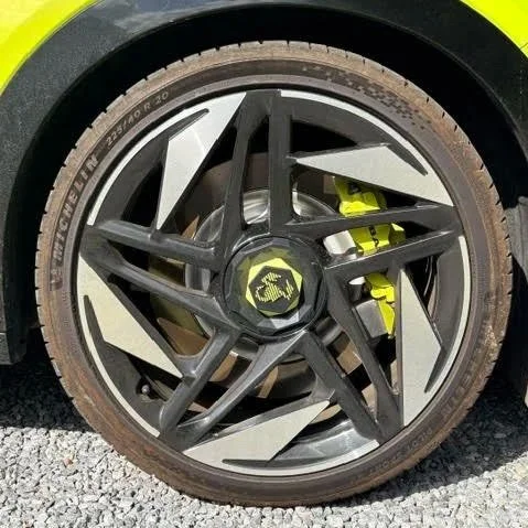 Close-up van een autoband met een opvallend zwart en zilverkleurig alloy velg en een gele remklauw erachter.