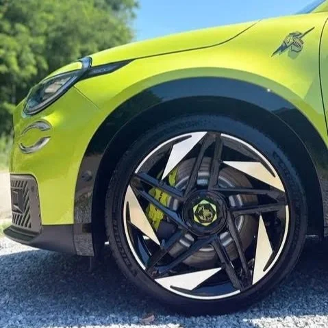 Close-up van de voorzijde van een limegroene sportwagen, gericht op het wiel met een zwart en wit spijlenpatroon en een logo in het midden.