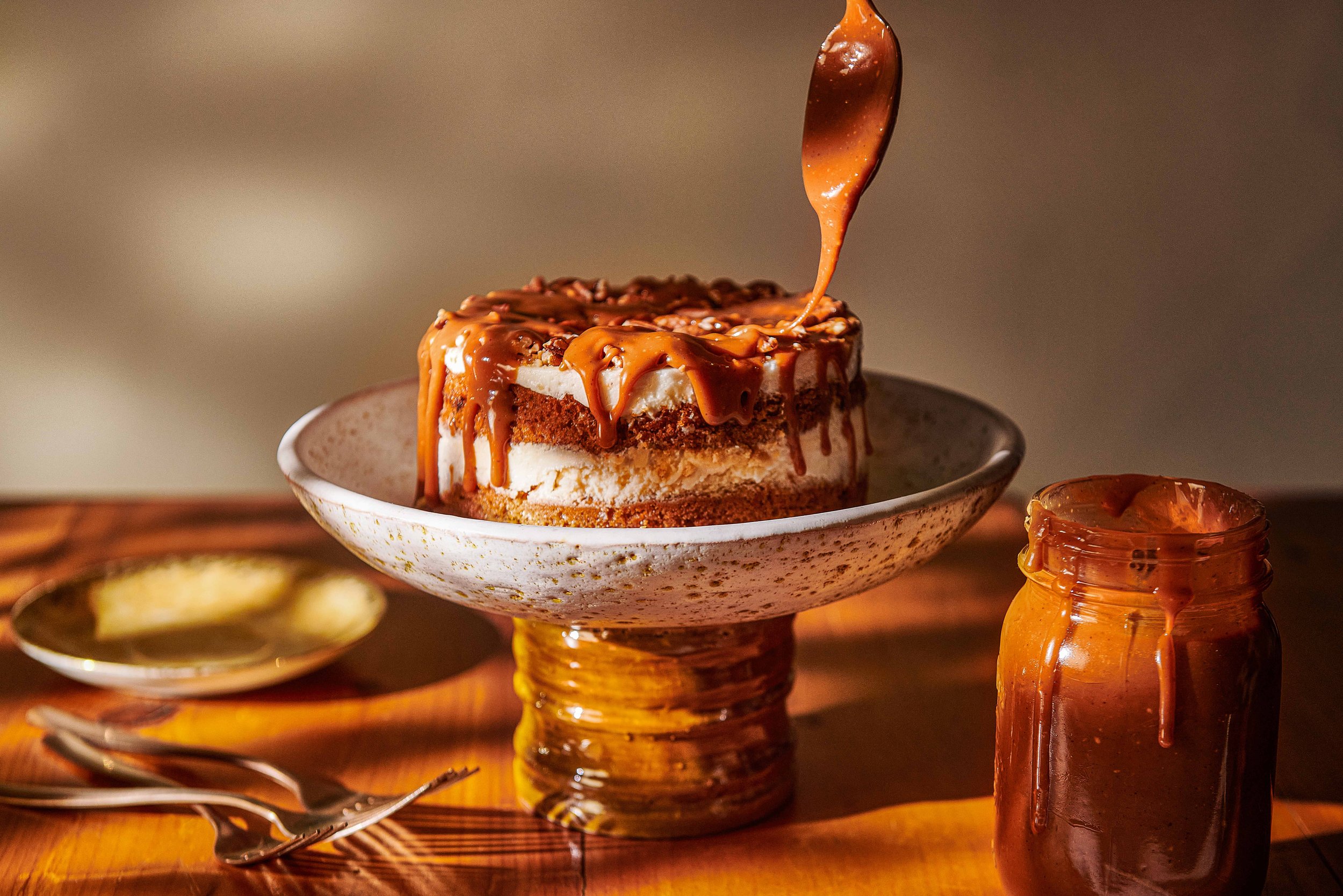  A generous pour of caramel drizzle is dropped onto a luscious carrot cake on a ceramic cake stand. The dappled light creates an autumnal mood for this food photograph created by El Keegan, Dublin, Ireland.  