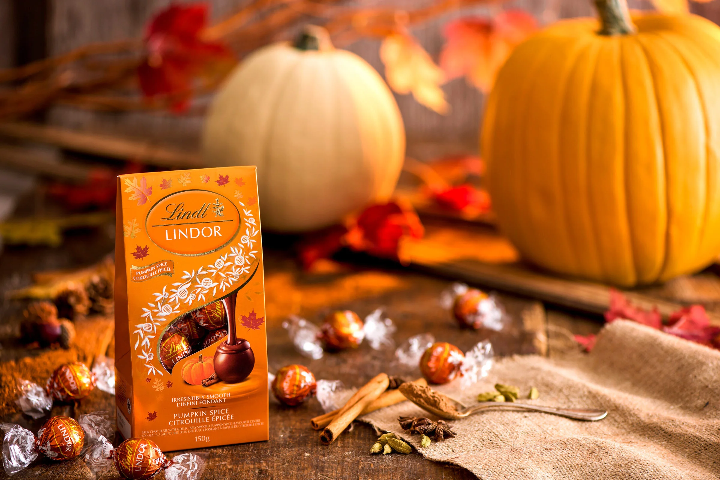  A packet of Pumpkin Spice Lindor balls sits on a rustic wooden surface with food flavour cues in the background including cinnamon and pumpkins. Autumnal photo created by Dublin Photographer El Keegan. 