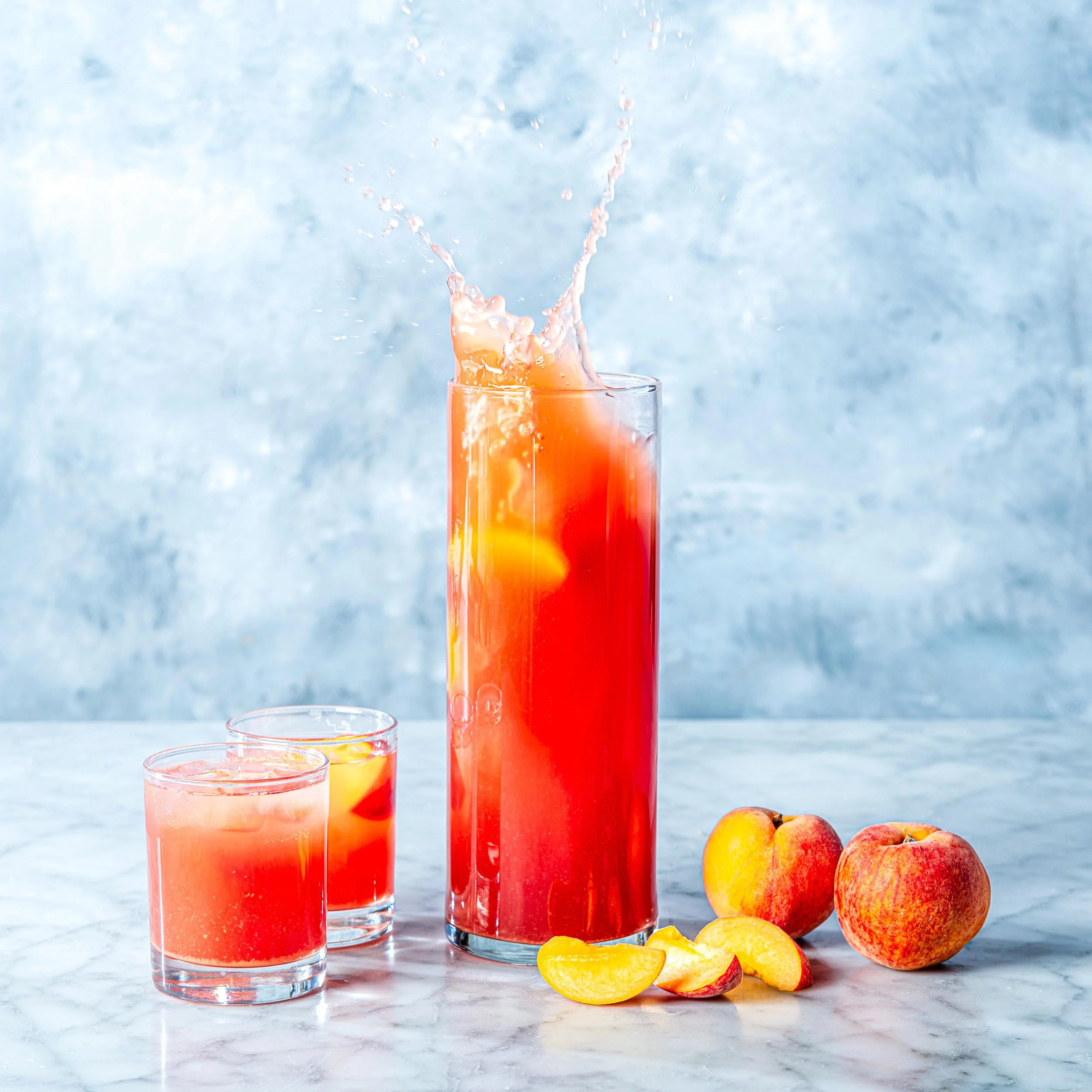  A large splash captured in a jug of peach drink with fresh peaches and two glasses. Action photography by Dublin Photographer and Retoucher El Keegan.  
