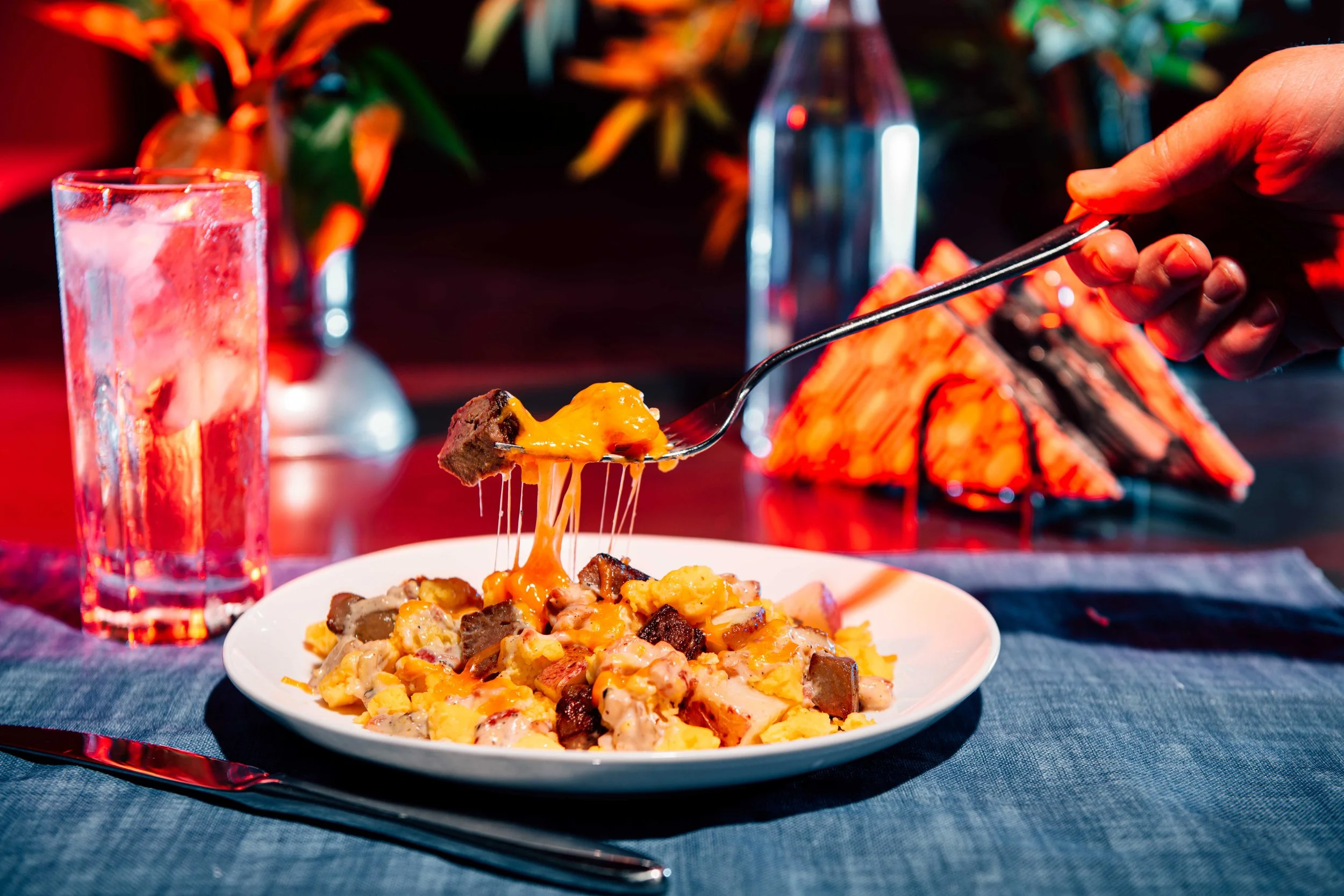  A hand holds a fork of melted mac and cheese in the neon glow of a diner. Commercial food photography by El Keegan, Dublin.  