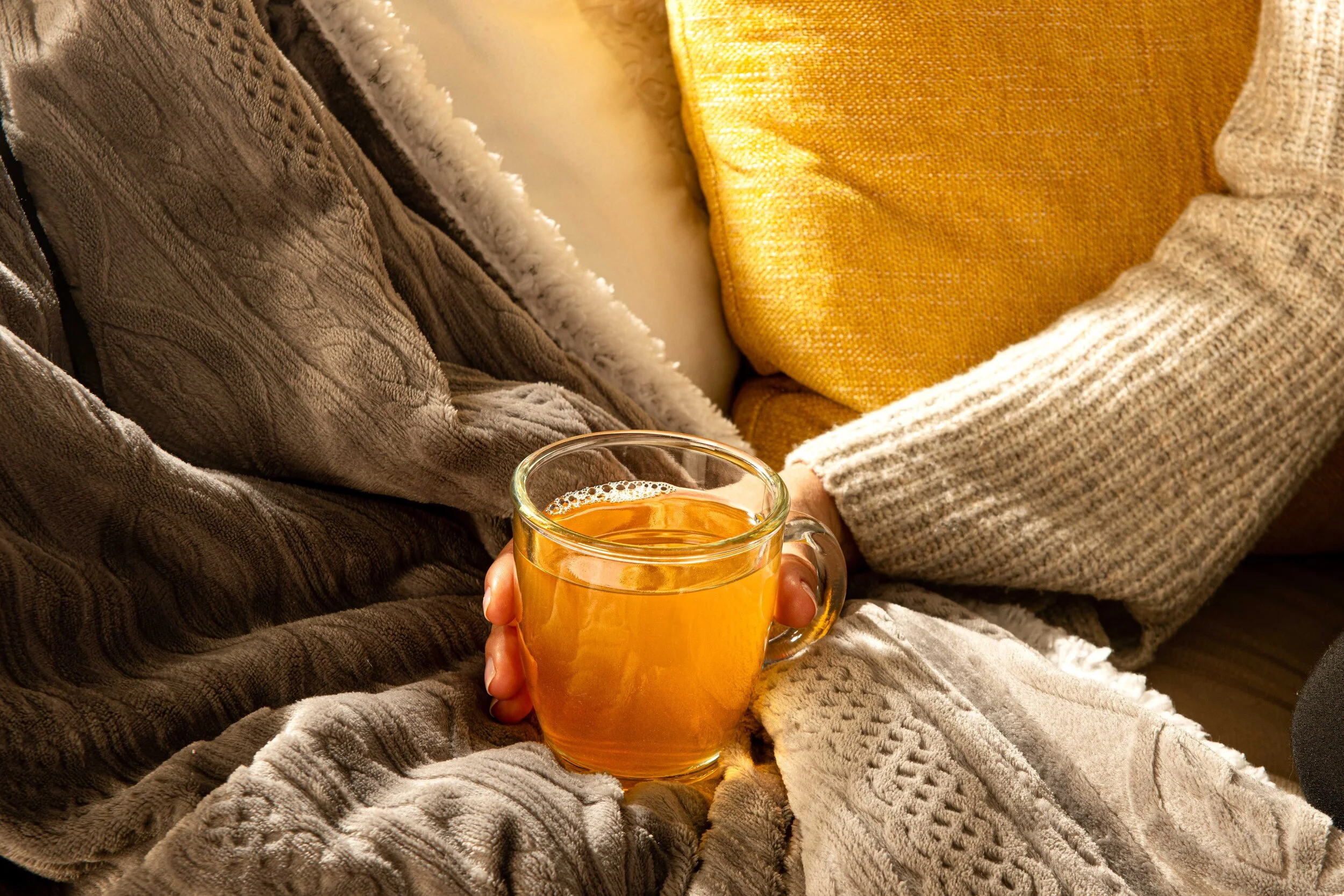  A person in a cosy woolen jumper holds a hot cup of tea in a glass mug. Photographed by El Keegan, Ireland.  